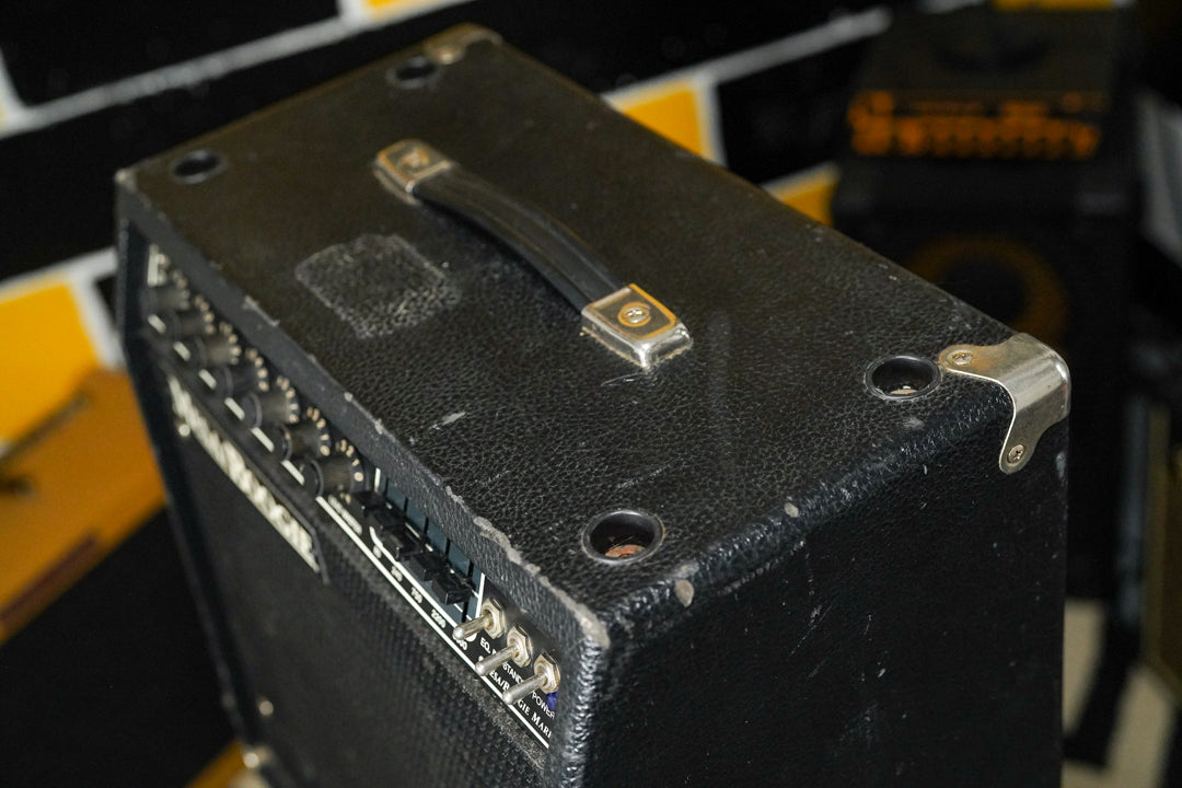 Overhead view of a black textured combo amp, showing the top handle, metal corner protectors, and front panel controls with wear.