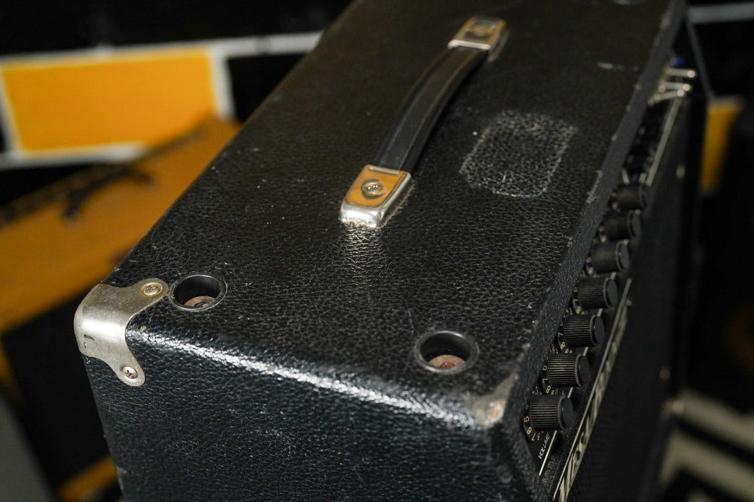 Top-down view of the black textured amp, showing the handle, a metal corner guard, and a row of black control knobs on the side.