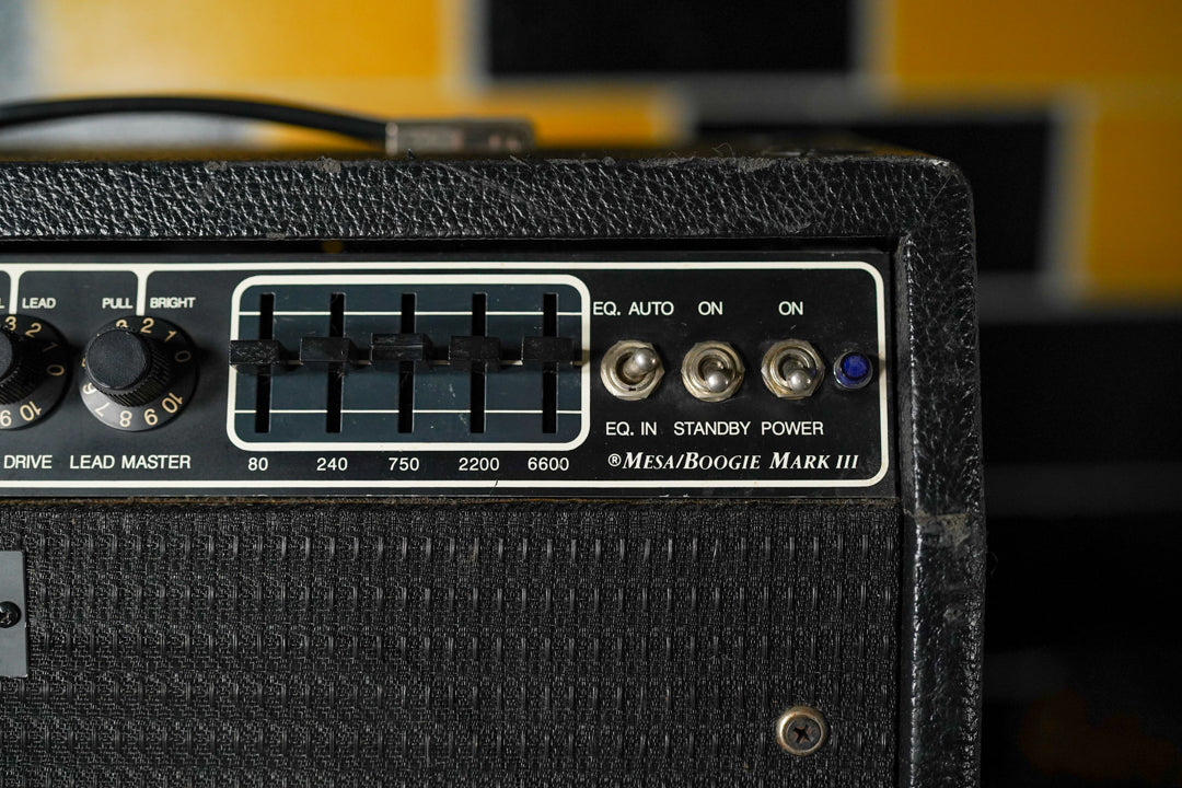 Close-up of the black textured amp's control panel, showing two knobs, a 5-band EQ, three toggle switches, and a blue power light.