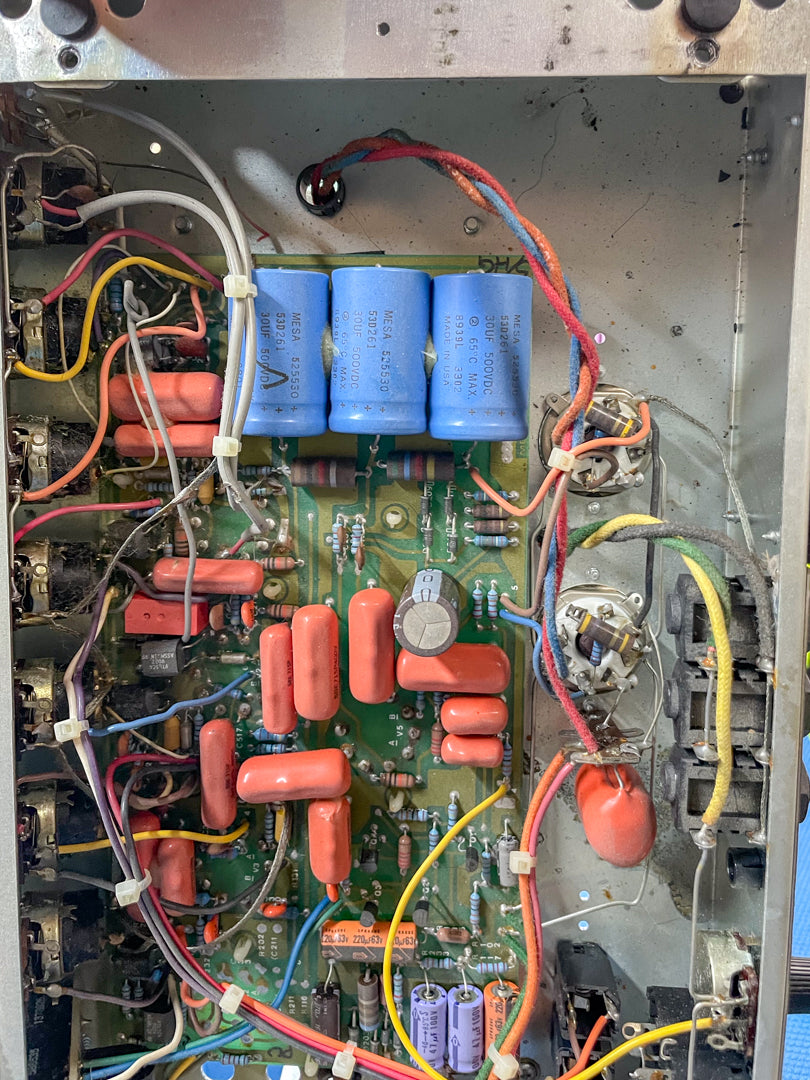 Overhead view of the amplifier's internal circuit board, showing numerous orange capacitors, blue filter caps, and wiring.