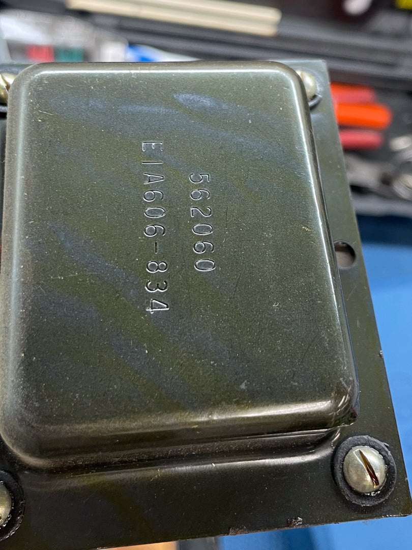 Close-up of a dark green transformer with "562060" and "E1A606-834" stamped on top, secured by two screws.