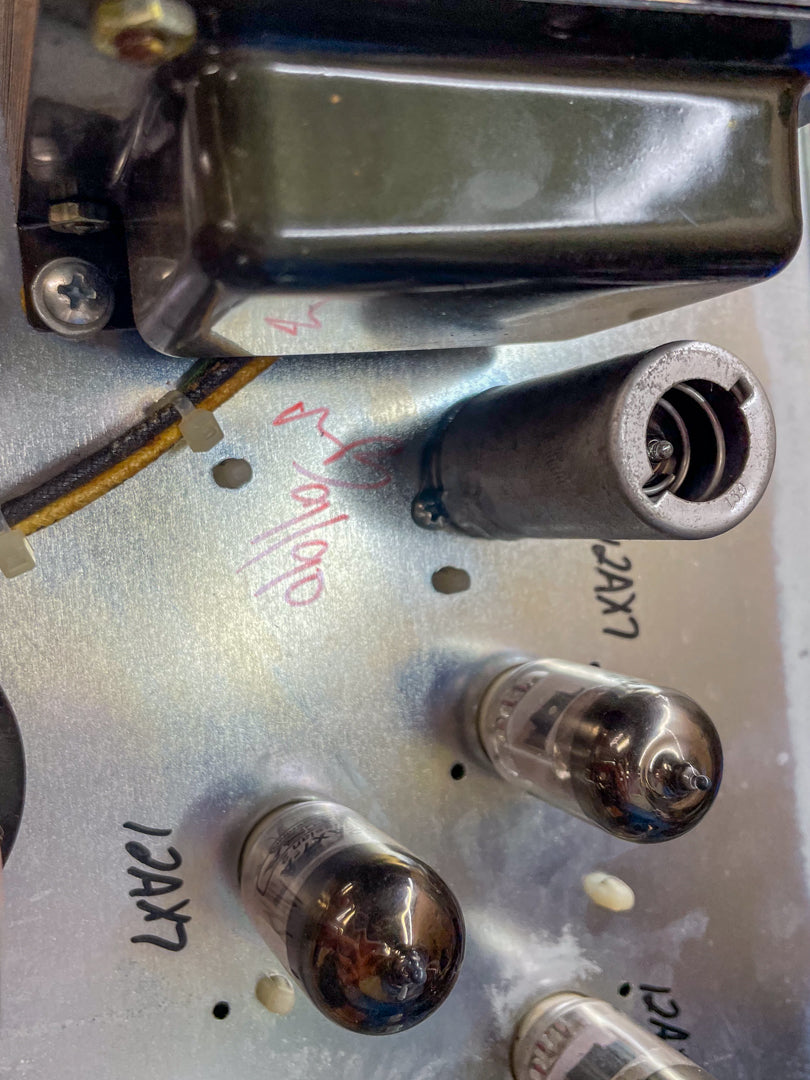 Close-up of the amp's internal chassis, showing three 12AX7 preamp tubes, a tube retainer, and a black transformer.
