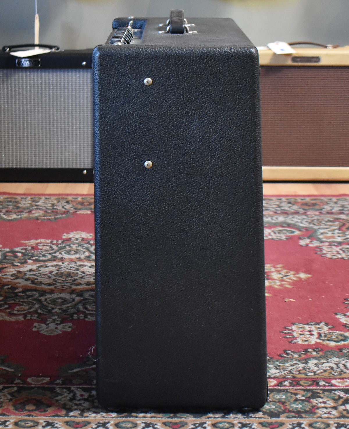 The black textured combo amp is seen from its right side, showing a top handle and two silver screws on the side.