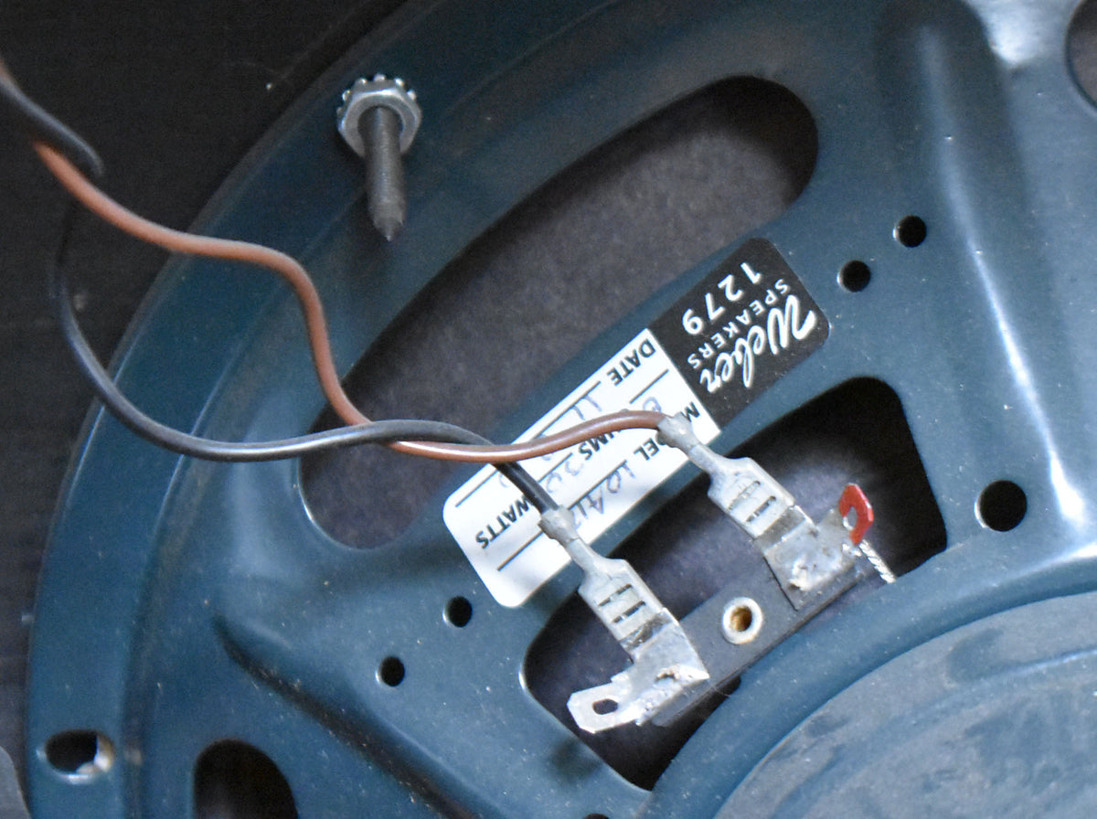 Close-up of a dark teal speaker frame with two wires connected to terminals, showing a white Weber Speakers label.
