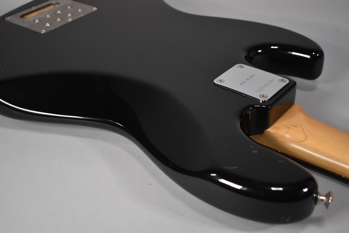 The bass's glossy black body, viewed from the back, shows a chrome neck plate and a rectangular control cavity cover.