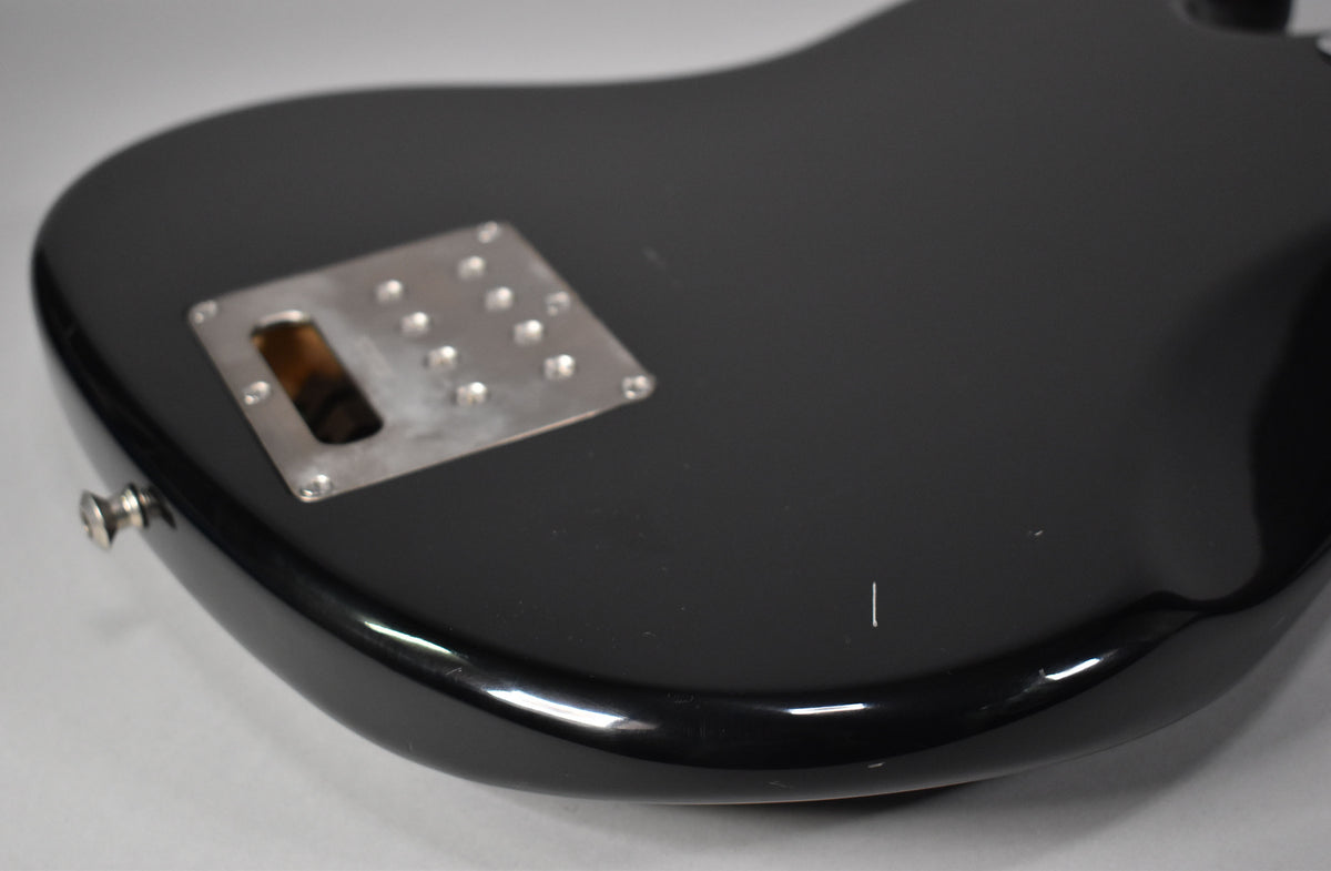 The black gloss bass body, viewed from the rear, shows a chrome neck plate with a rectangular opening and a small scratch on the lower bout.