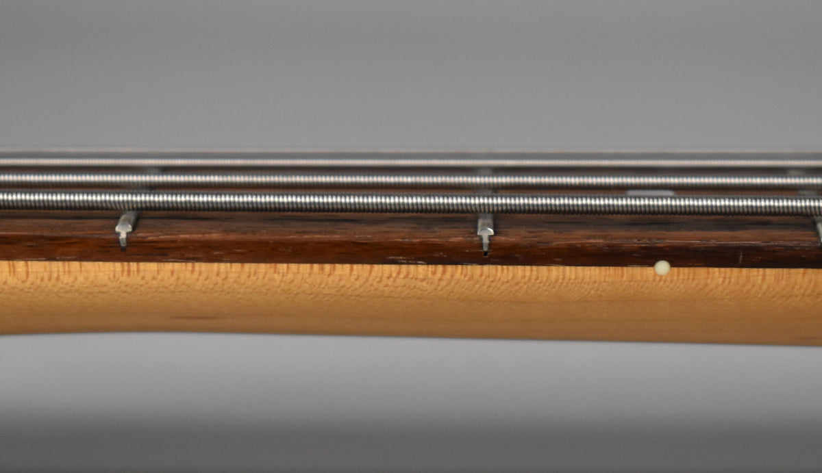 Close-up of the bass neck's side, showing a dark rosewood fretboard, maple neck, and a white side dot marker.