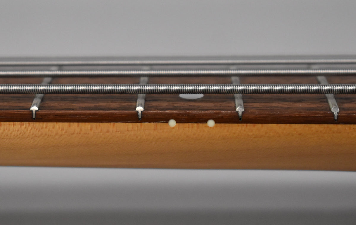 Close-up of the bass neck's side, showing the light maple finish, dark fretboard, and two cream-colored side dots.