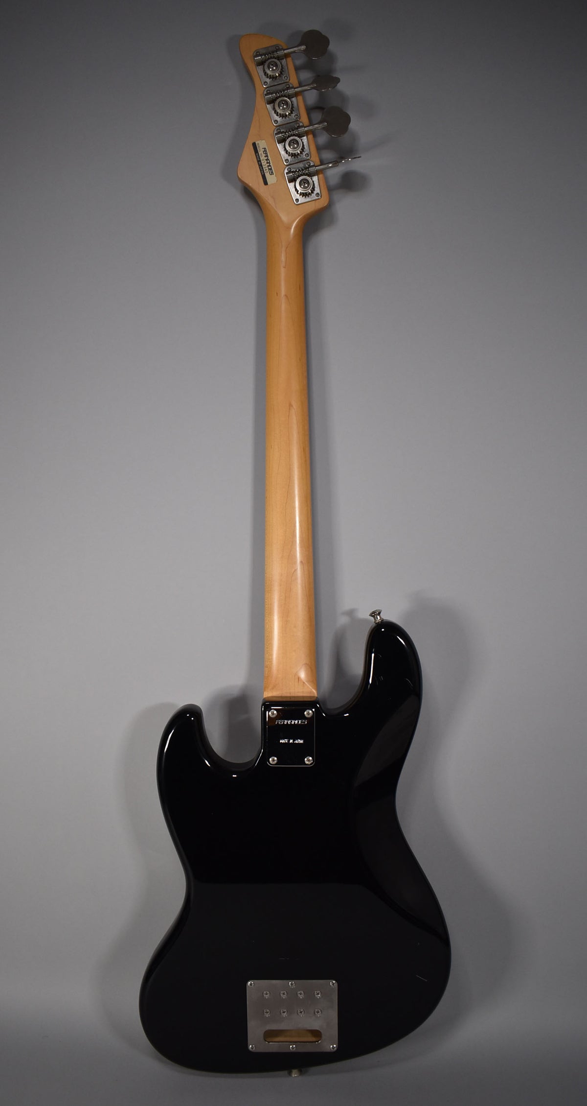The black gloss bass is shown from the back, revealing a light maple neck, chrome tuners, and a rectangular chrome control plate.