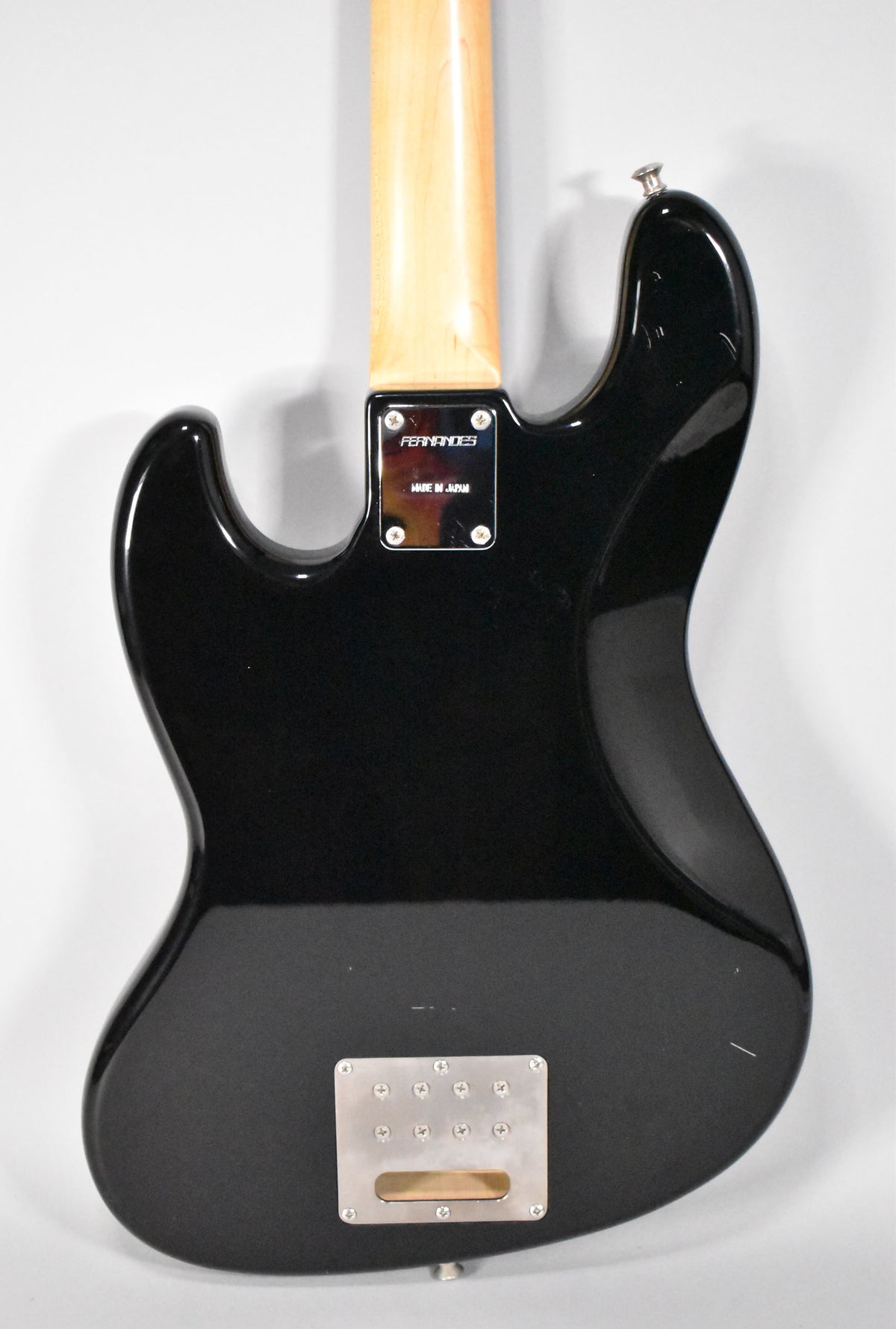 The back of a black bass guitar, showing a maple neck, a chrome neck plate, and a rectangular chrome string-through-body plate.