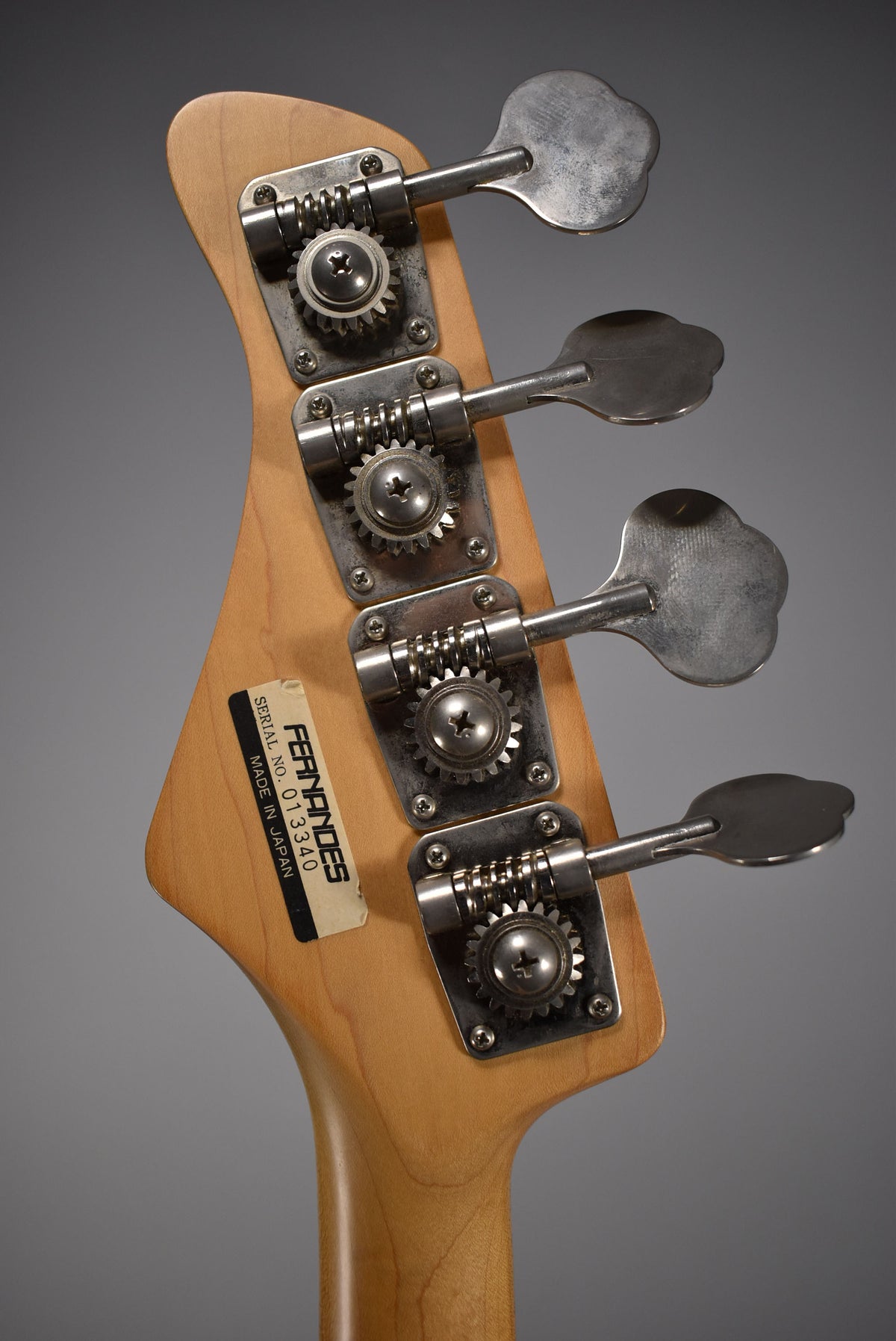 The back of a light wood headstock with four worn, tarnished chrome tuning machines and a faded "Made in Japan" sticker.