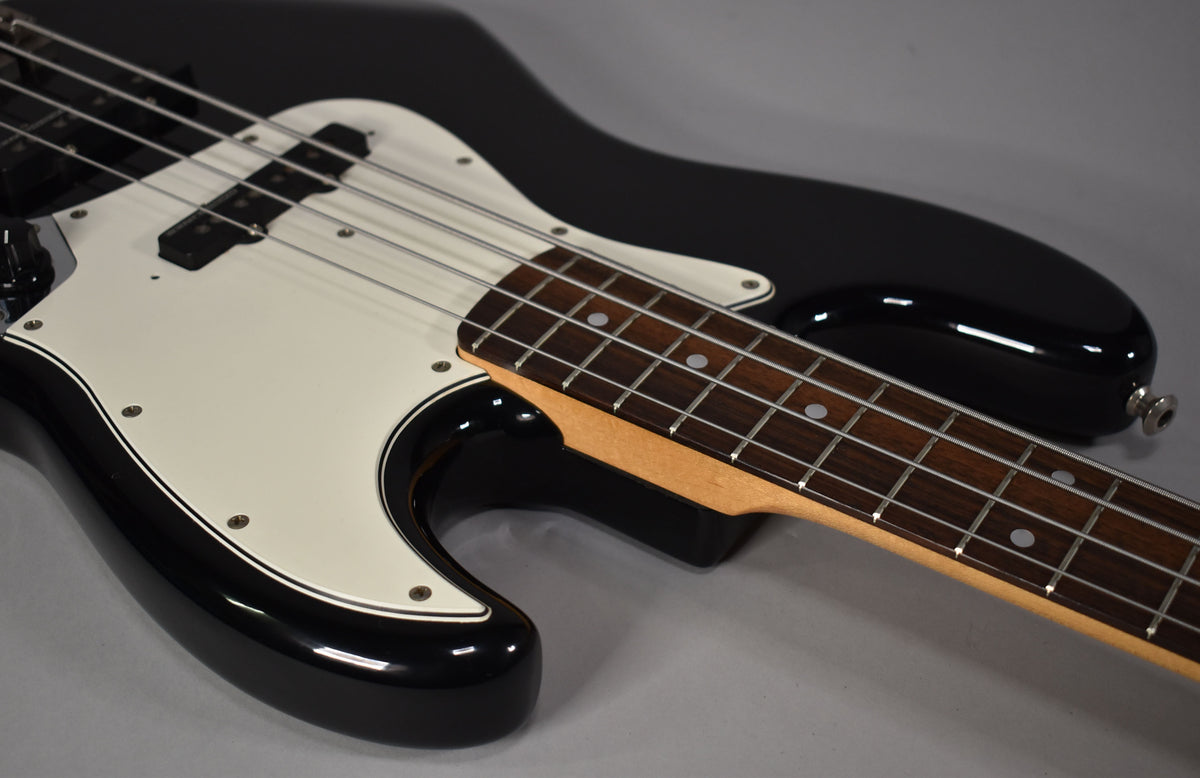 Close-up of a black gloss bass guitar with a white pickguard and split-coil pickup, showing the rosewood fretboard with dot inlays.