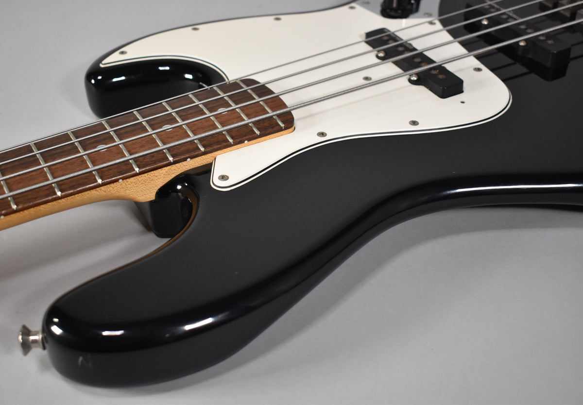 Upper body of a black gloss bass, angled from the lower bout, showing the white pickguard, two single-coil pickups, and rosewood fretboard.