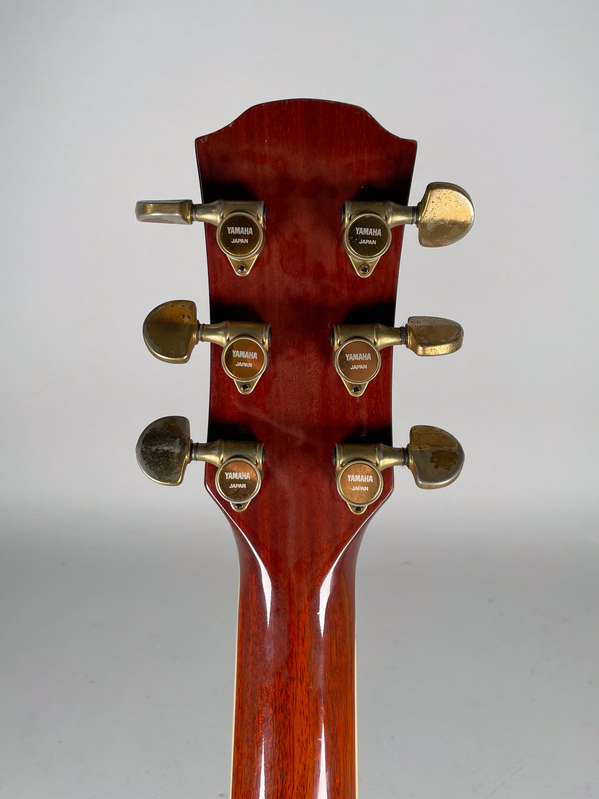 Rear view of the guitar's headstock and neck, showing six gold-toned tuners with visible tarnishing and wear on the buttons.