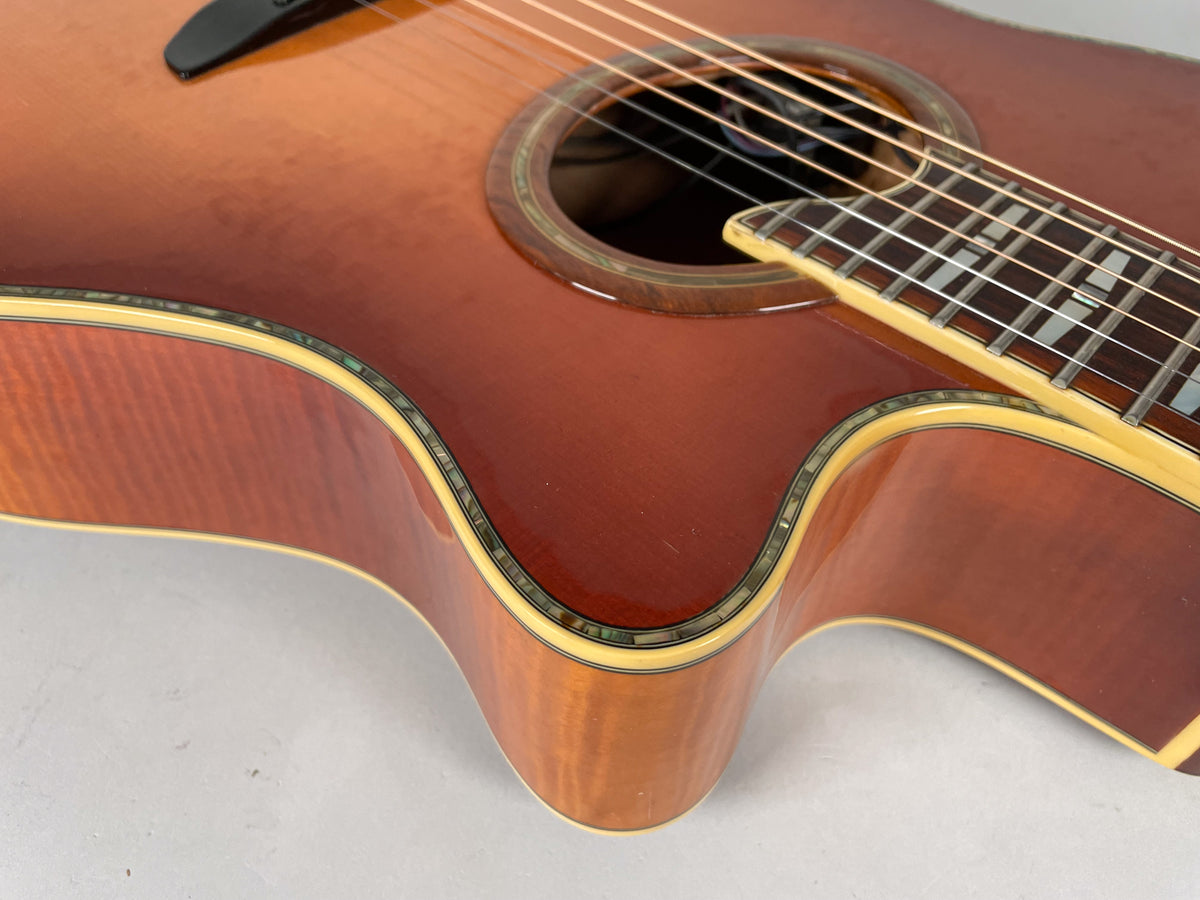 Close-up of the sunburst acoustic guitar's lower bout and cutaway, showing abalone binding, a dark soundhole rosette, and block inlays.