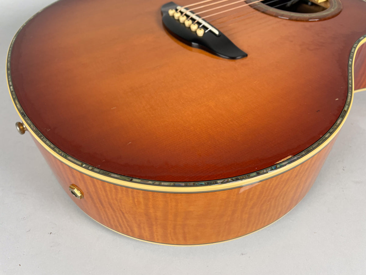 Close-up of the guitar's lower bout, showing the sunburst top, abalone binding, flame maple side, and a few small dings.