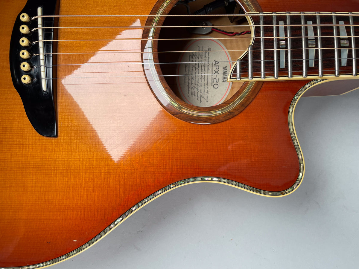 Close-up of the sunburst acoustic guitar's body, showing the bridge, soundhole, lower fretboard, and cutaway with mother-of-pearl binding.