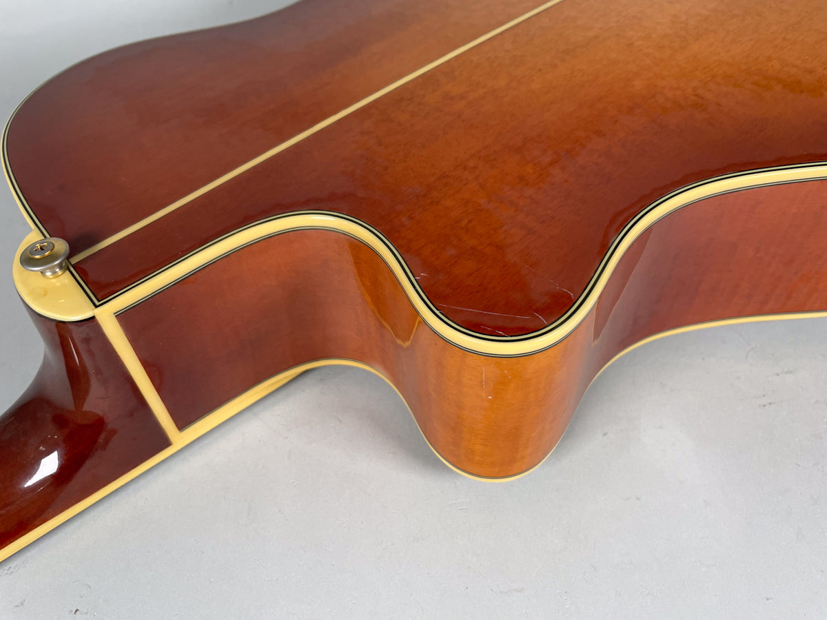 The sunburst acoustic guitar's lower bout and cutaway, showing a strap button and a visible scratch on the glossy finish.