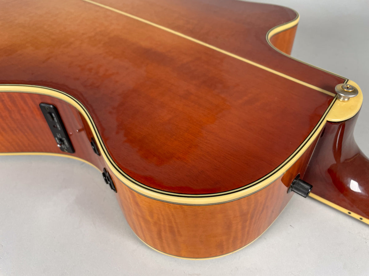Upper bout of a sunburst acoustic guitar, showing the glossy top, side-mounted preamp controls, and strap button.
