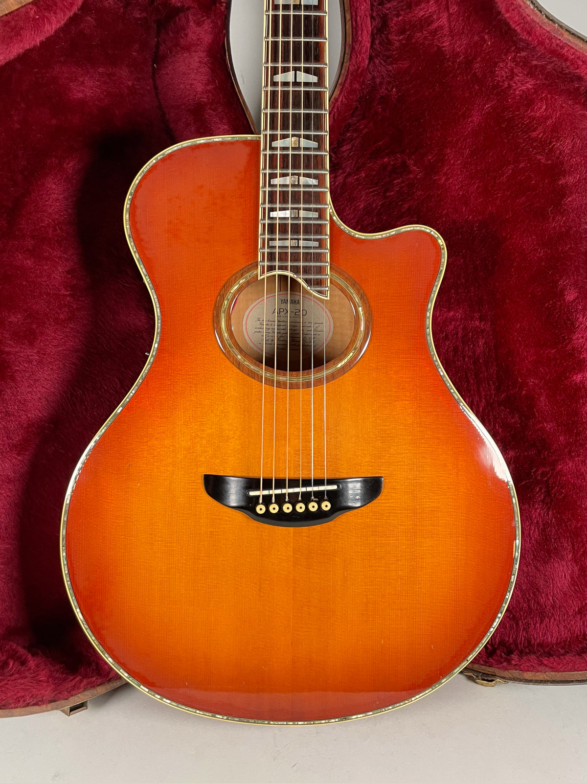 The sunburst acoustic guitar, with a cutaway and black bridge, is framed from the neck to the lower bout, resting in a red velvet case.