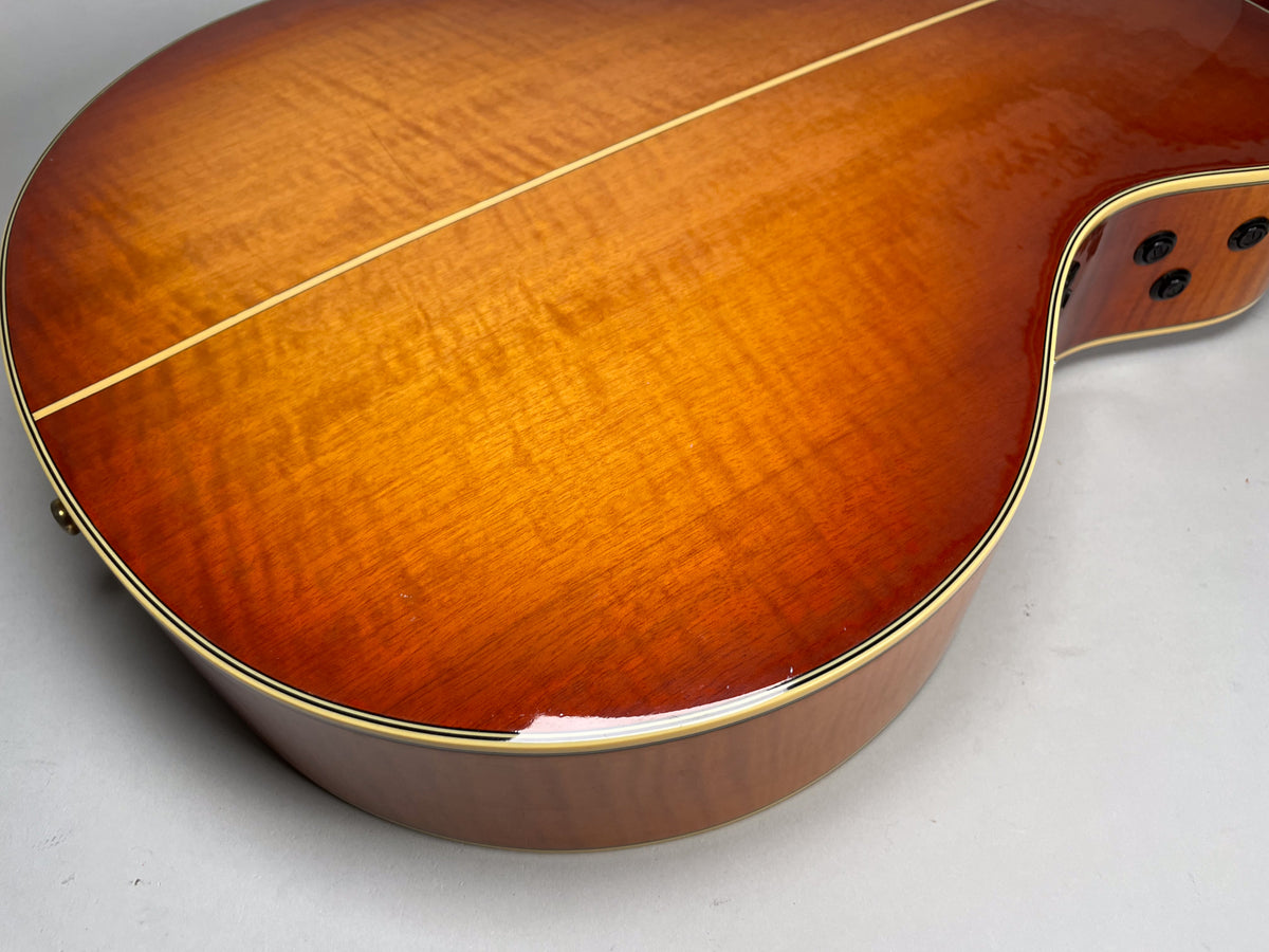 Close-up of a sunburst acoustic guitar's back, showing a flame maple pattern, a light center stripe, and part of the cutaway.