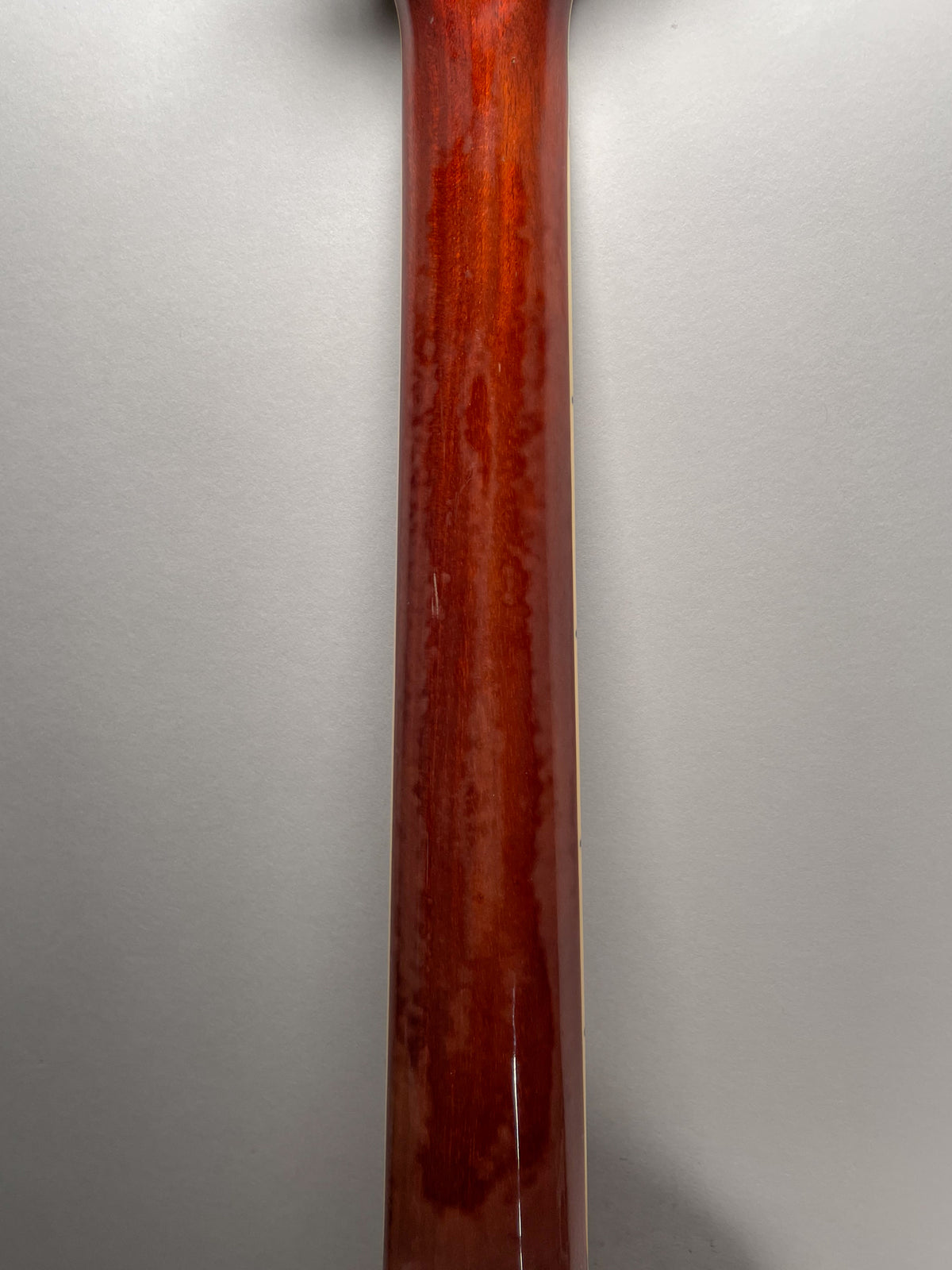 The guitar's neck, viewed from behind, shows a glossy reddish-brown finish with visible wood grain and a few light scratches.