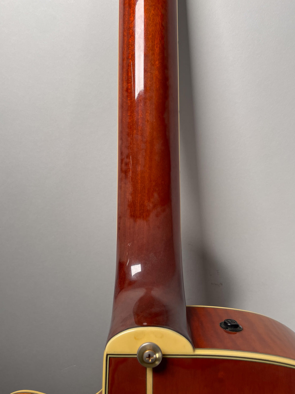 The guitar's glossy sunburst neck and body join, showing a strap button and a small black control knob, with minor finish wear.