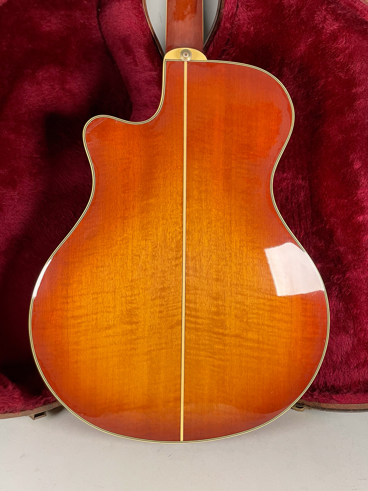 The guitar's sunburst back, with a visible wood grain and center seam, is framed in a red velvet case.