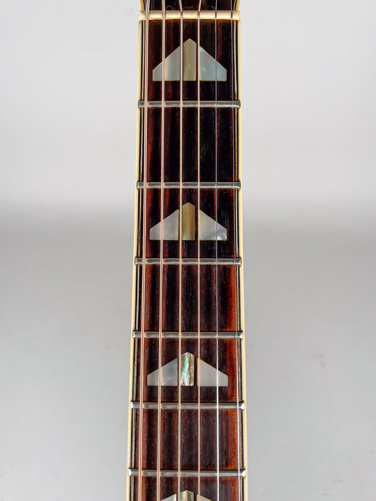 The dark rosewood fretboard is centered, showing six strings and mother-of-pearl split-triangle inlays.