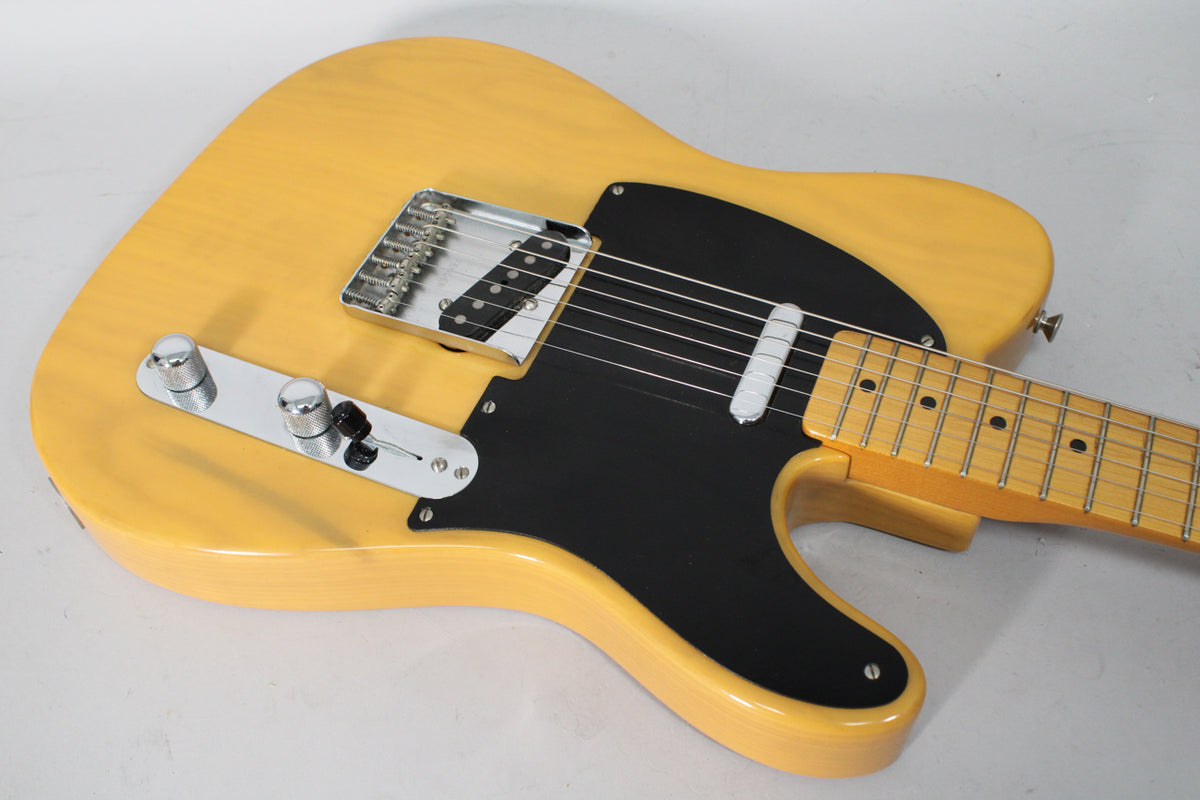 The butterscotch blonde Telecaster body is angled, showing its black pickguard, chrome bridge, control plate, and maple neck.
