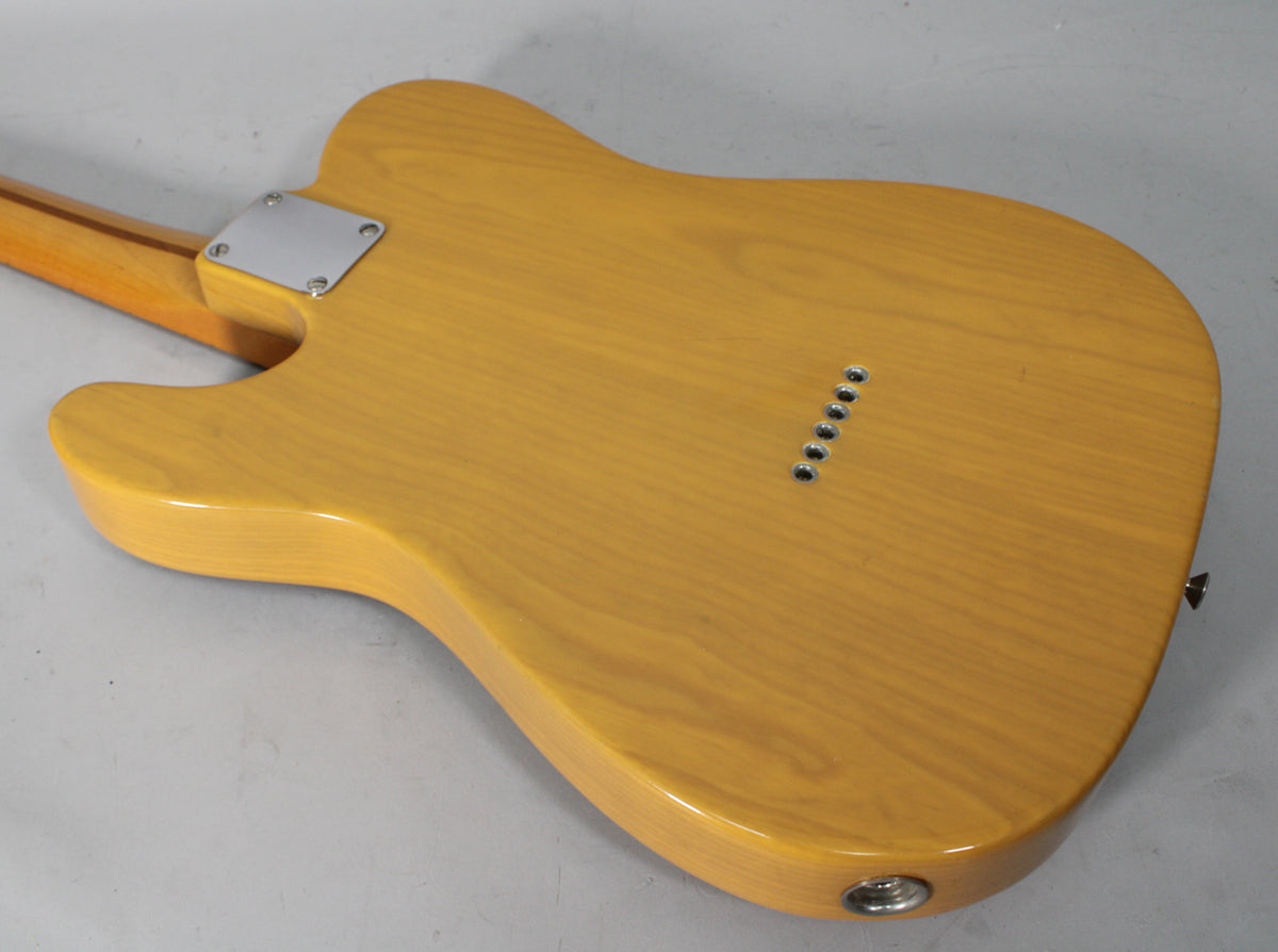 The guitar's butterscotch blonde back shows wood grain, a chrome neck plate, six string-through-body ferrules, and an output jack.