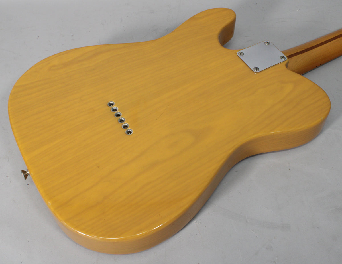 The guitar's butterscotch blonde body, viewed from the back, shows six string-through-body ferrules and a chrome neck plate.