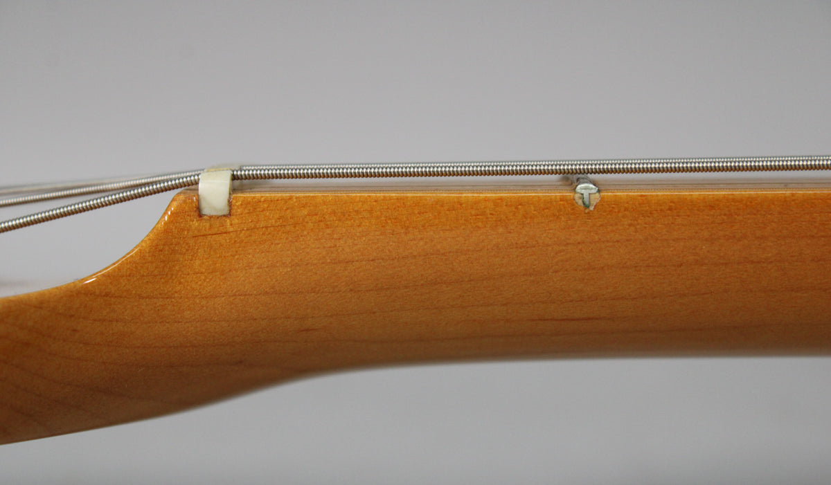 Close-up of the guitar's nut and first fret, showing the light blonde maple neck with a string tree and some minor wear.