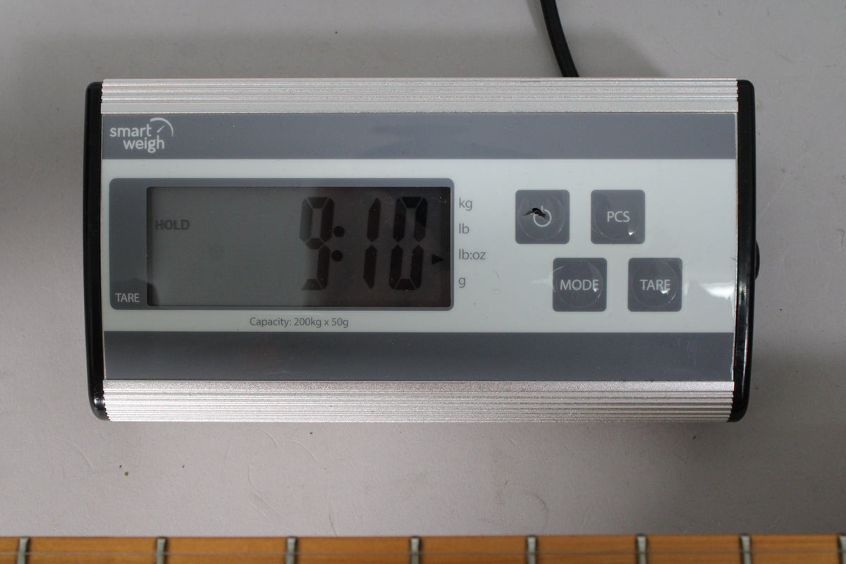 A digital scale displays "9.10" in black digits on a grey screen, with the bottom of a guitar neck visible below.
