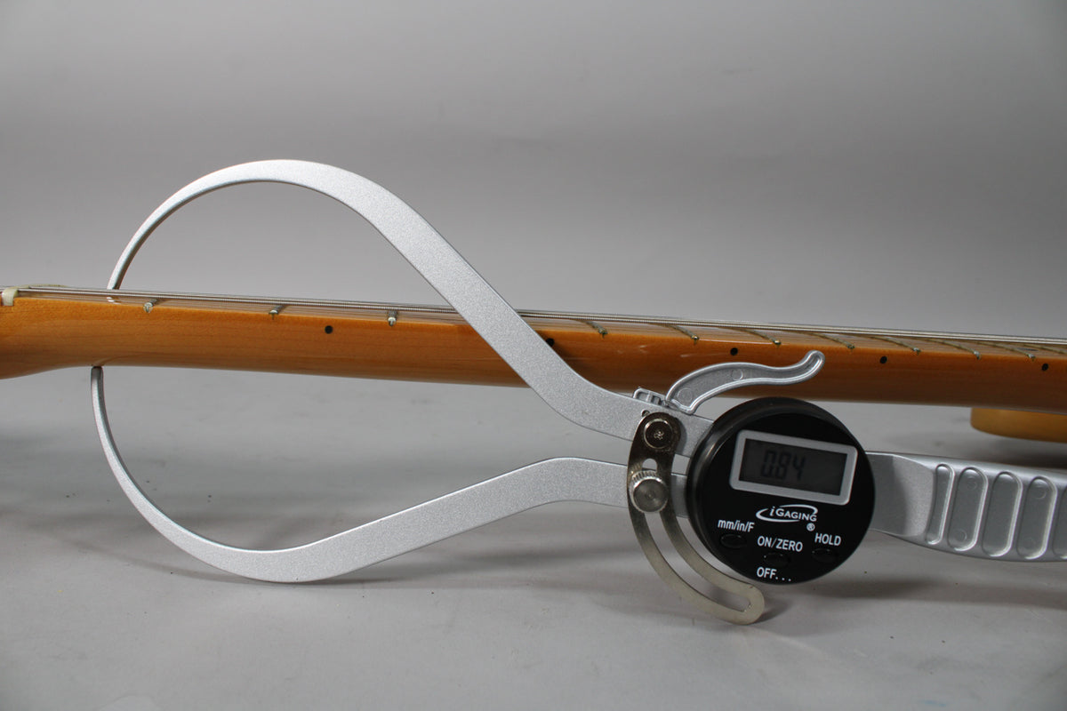 A digital caliper measures the guitar's maple neck, showing a reading of 0.84, with light wear on the fretboard.