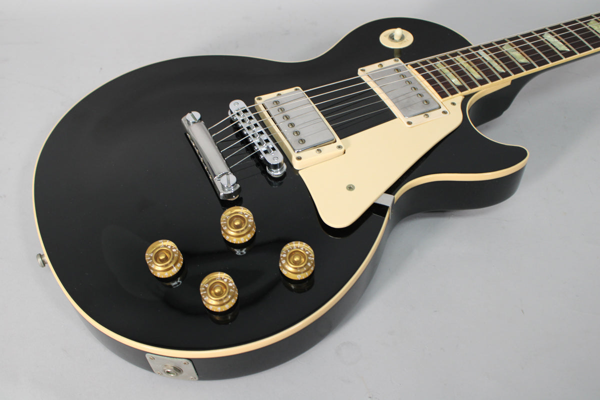Ebony black electric guitar, angled from the lower bout, showing cream binding, pickguard, and gold top hat knobs.