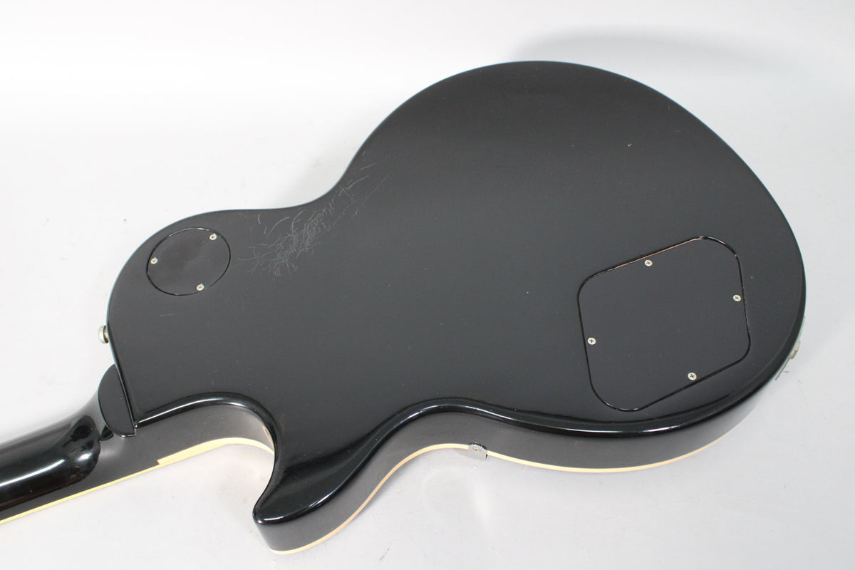 The back of the black guitar body shows a control cavity cover, a circular access plate, and light scratches on the upper bout.