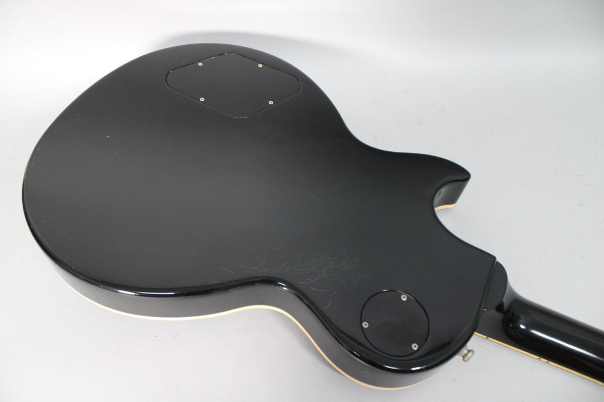 The back of the black guitar body shows light scratches and two control cavity covers, with a cream binding along the edge.