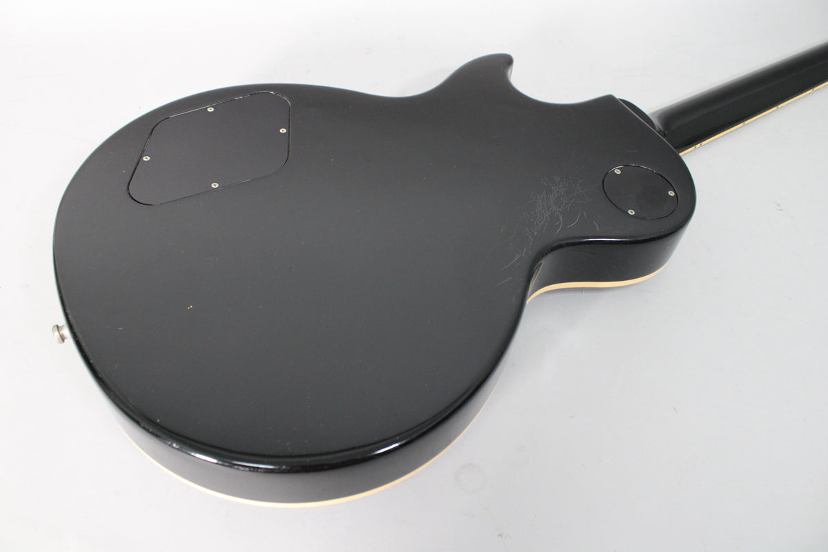The back of the glossy black guitar body, showing control cavity covers, cream binding, and light finish wear near the cutaway.