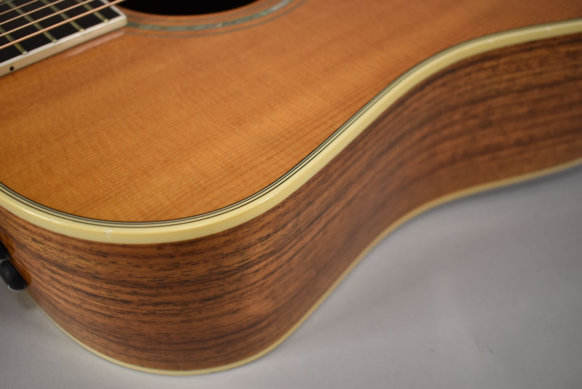 Close-up of the guitar's lower bout, showing the light brown top, dark brown wood grain side, and cream binding with thin black lines.