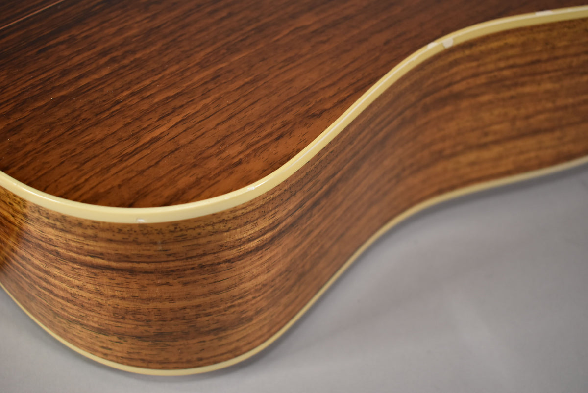 Close-up of the guitar's lower bout, showing the dark wood grain, light binding, and a small chip on the top edge.
