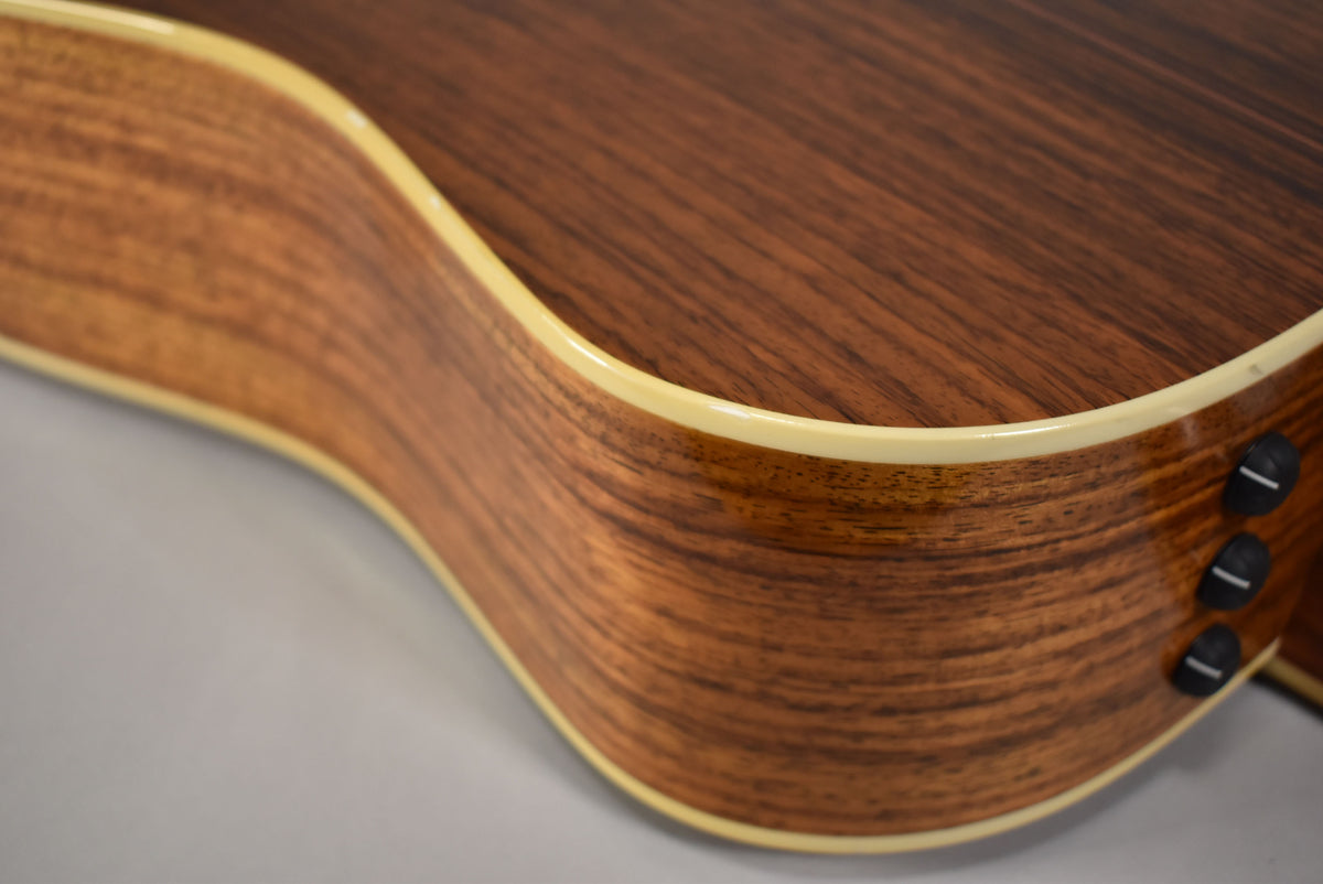 Close-up of the guitar's lower bout, showing the dark brown wood grain, light binding, and three black control knobs on the side.