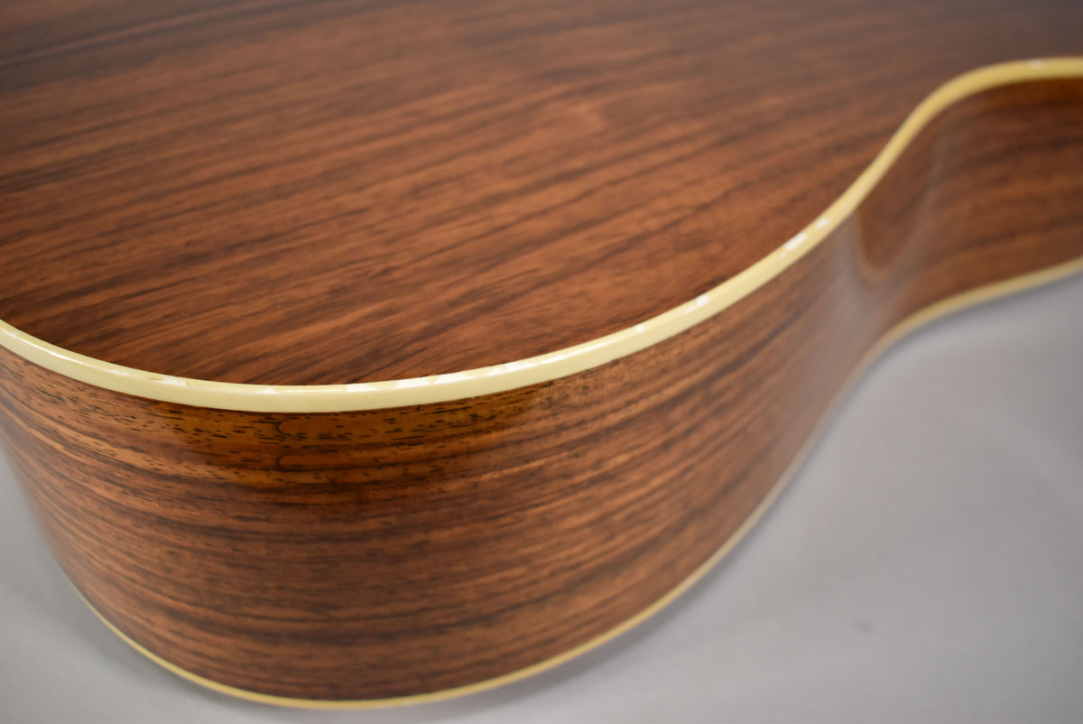Close-up of the guitar's lower bout, showing the natural wood grain, light binding, and a slight curve of the body.