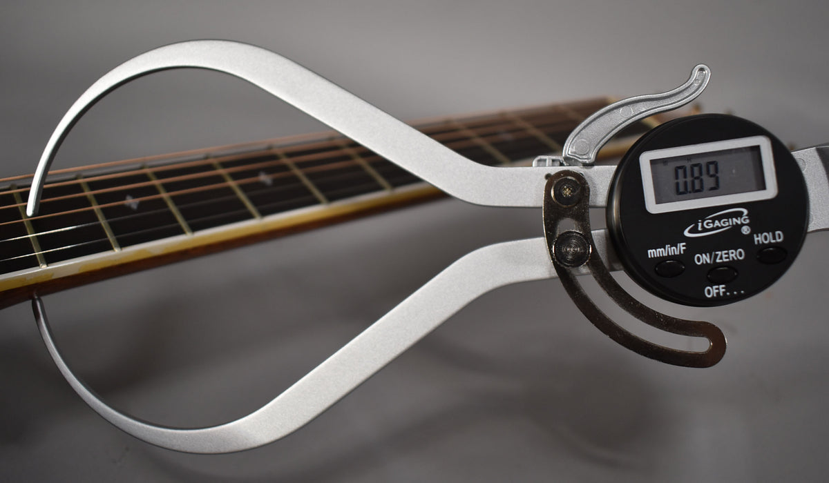 A digital caliper measures the guitar's neck relief at the 7th fret, displaying 0.89mm, with the fretboard and strings visible.