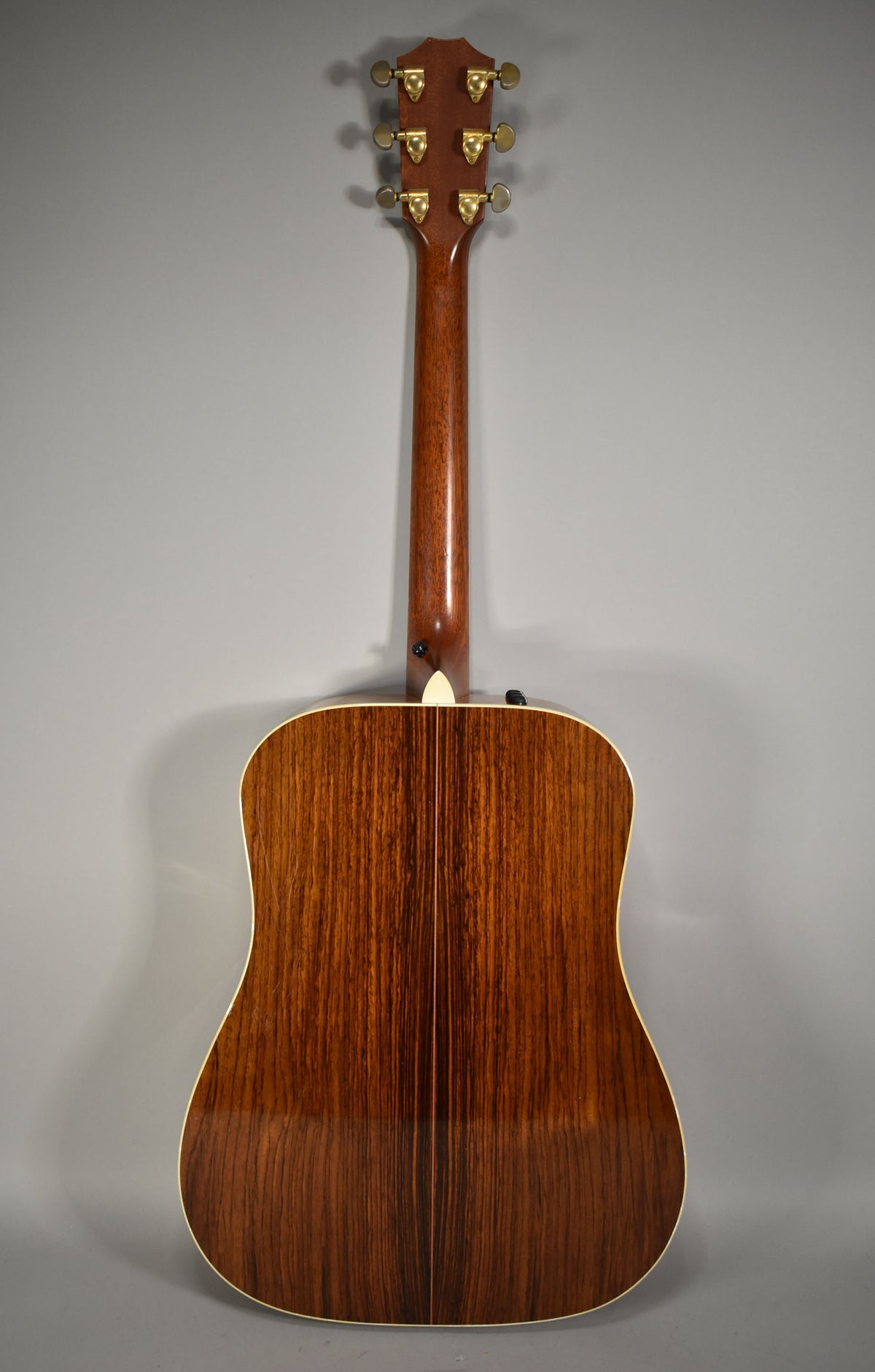 The guitar's back, neck, and headstock are visible, showing a dark brown wood grain with a glossy finish and gold tuners.