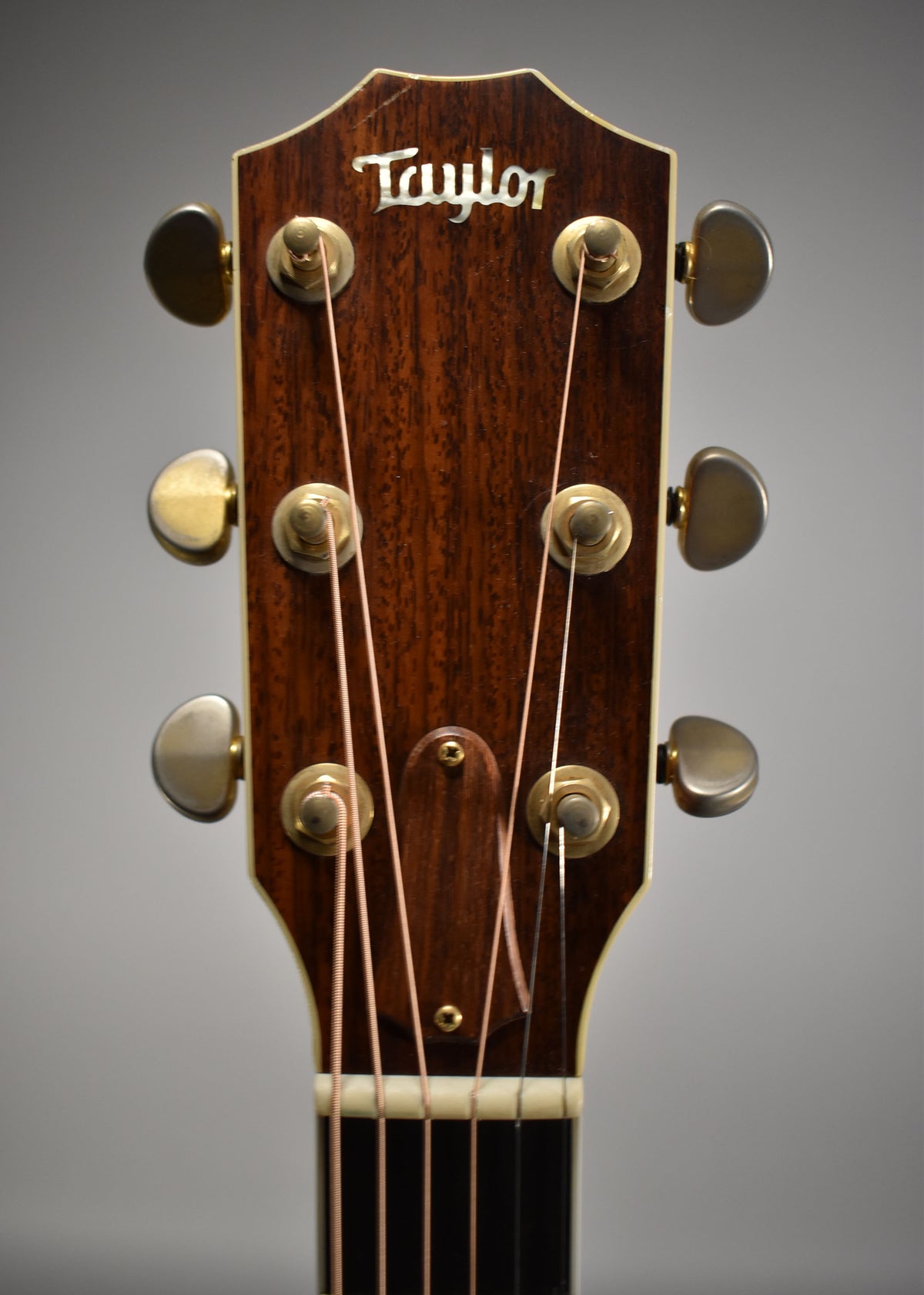 Close-up of the guitar's dark brown headstock with a natural wood grain, showing six gold-toned tuners and light wear.