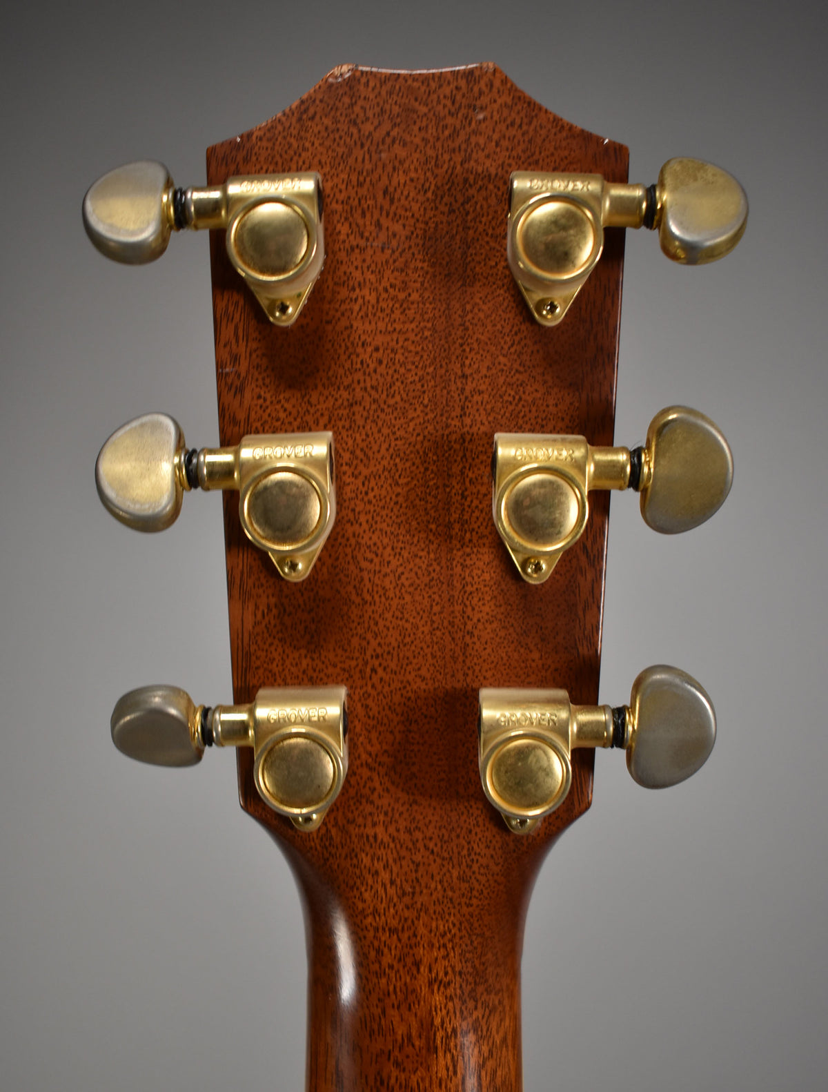 The back of the guitar's headstock and neck, showing six gold-toned tuning machines on a rich brown wood finish.