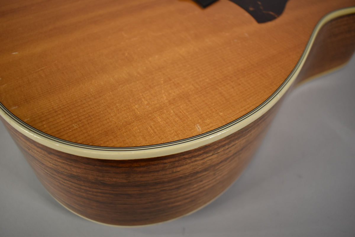 Close-up of the guitar's lower bout, showing the natural wood grain, cream binding with black pinstripes, and light surface wear.