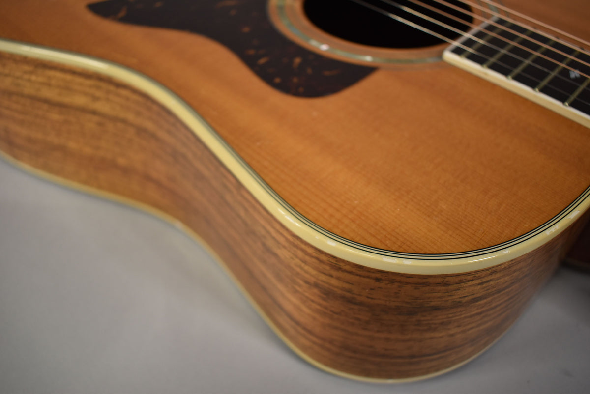The upper bout of a natural finish acoustic guitar, showing the light wood grain of the top and striped sides.