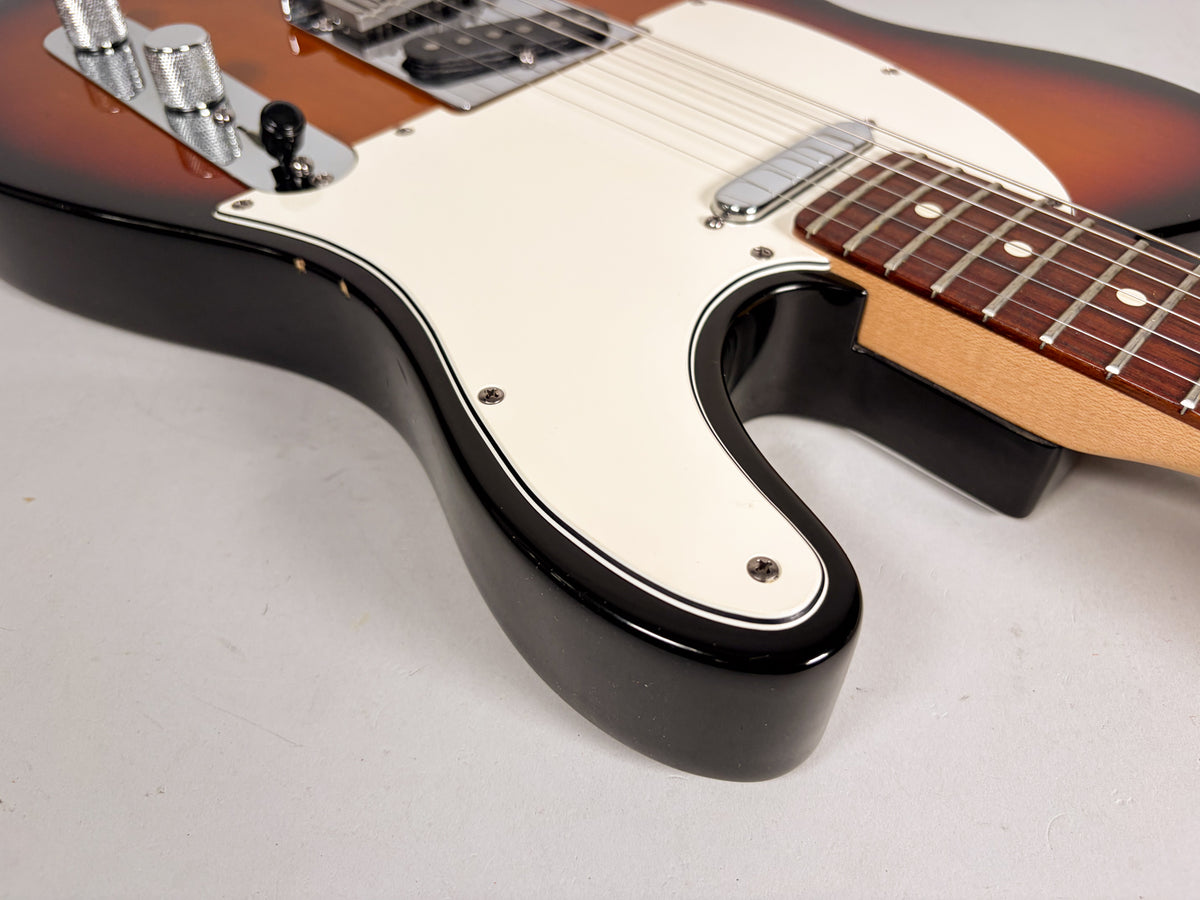 Close-up of the Telecaster's lower body, showing the sunburst finish, cream pickguard, chrome control plate, and rosewood fretboard.
